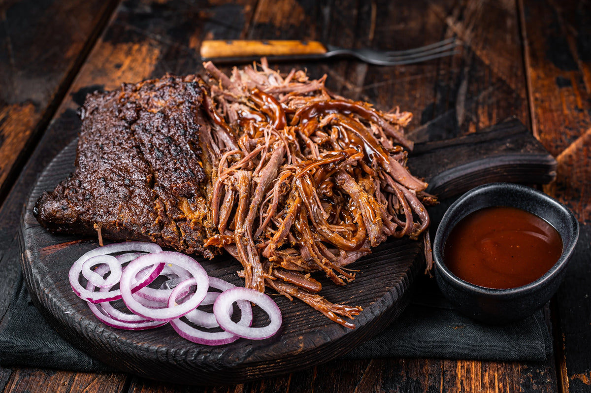 Slow-cooked Bromfields Pork Boston Butt with BBQ sauce and red onion rings on a wooden board