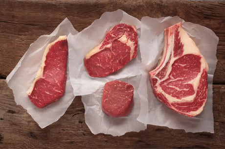 Assorted premium raw Welsh beef cuts on white parchment paper over a rustic wooden background