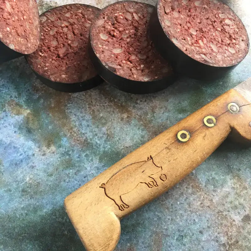 Freshly sliced black pudding rounds next to a wooden knife with pig engraving on the handle.