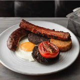 delicious plate featuring black pudding, sausages, a fried egg, grilled tomato, and savory sides on a rustic table.