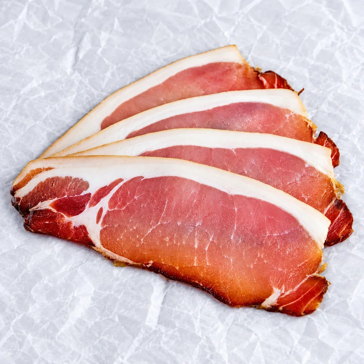 Thin slices of Bromfields Bacon oak smoked bacon on white parchment paper