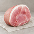 A raw Bromfields Gammon horseshoe joint tied with red netting on white parchment paper.