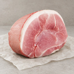 A raw Bromfields Gammon horseshoe joint tied with red netting on white parchment paper.