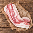 Fresh Bromfields Bacon streaky pork belly on brown parchment paper over a rustic wooden surface