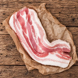 Fresh Bromfields Bacon streaky pork belly on brown parchment paper over a rustic wooden surface
