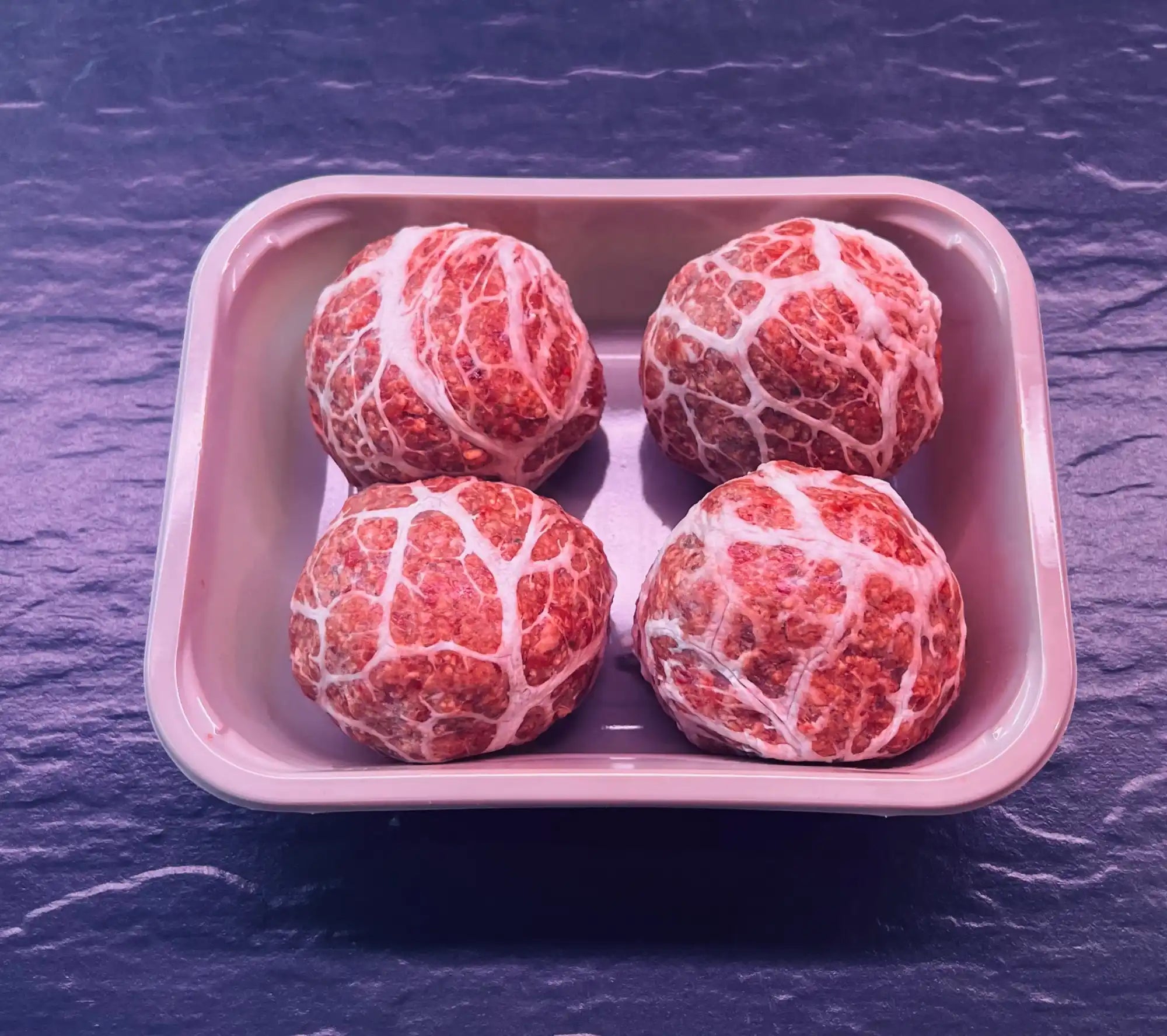 Four raw, marbled beef meatballs in a pink tray.