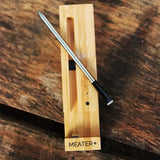 MEATER Plus smart thermometer on a wooden surface, showcasing its sleek design and precision sensor.