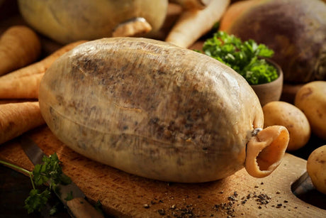 Traditional haggis displayed on a wooden board surrounded by fresh vegetables and herbs.