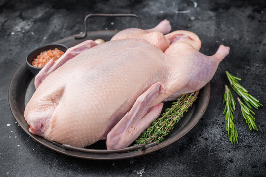 Whole raw Bromfields Game duck on a dark metal tray with rosemary and salt.